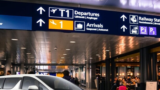 An airport departures sign with directions to T1, Arrivals, and Railway Station.