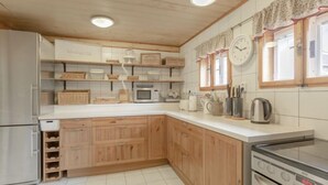 Une cuisine avec des meubles de rangement en bois, un réfrigérateur en acier inoxydable, un four à micro-ondes, une cuisinière et une horloge murale.