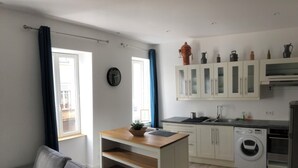 A modern kitchen with white cabinets, a built-in washing machine, and a wooden dining table. - Appartement Centre de Trévoux (Trévoux)