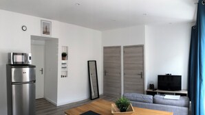 A modern living space with a dining area, a kitchen with a stainless steel refrigerator, a grey sofa, a TV, and a large mirror. - Appartement Centre de Trévoux (Trévoux)