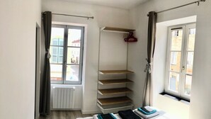 A bedroom with a bed, a window, a radiator, a shelf, and a hanging garment rack. - Appartement Centre de Trévoux (Trévoux)