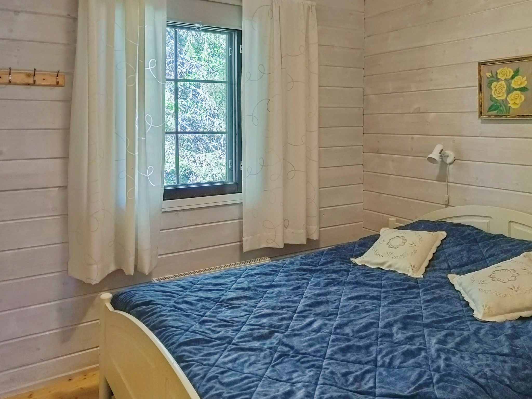 A bedroom with a bed, a window with curtains, and a wall-mounted light fixture.