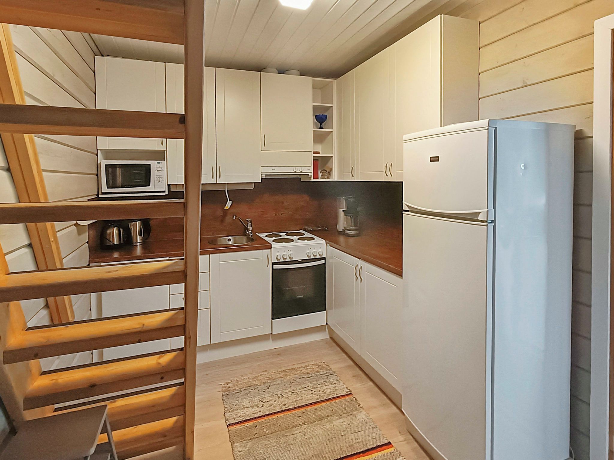 A compact kitchen with white cabinets, a microwave, a stove, and a refrigerator.