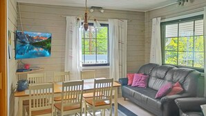 Kodikas olohuone, jossa on musta nahkasohva, puinen ruokapöytä ja tuolit. Seinälle on asennettu televisio, ja huoneessa on ikkuna, jossa on verhot.