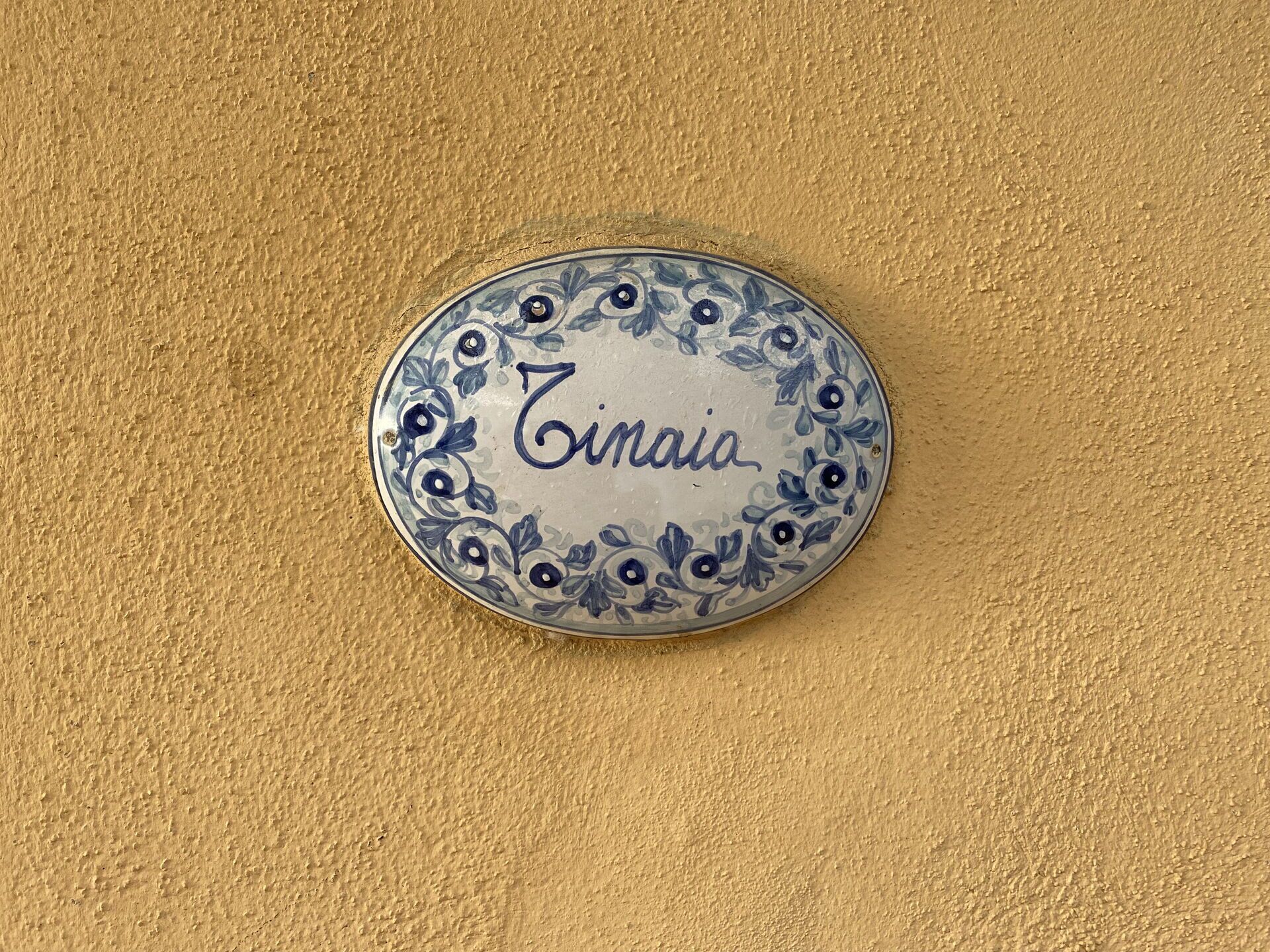 A round, decorative plate with the name "Zinaia" on it, placed on a textured beige surface.