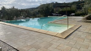 Ein rechteckiger Pool mit Fliesen umgeben, mit Liegestühlen und einer Pergola.