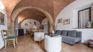 Ein Wohnzimmer mit Ziegeldecke, einem grauen Sofa, einem weißen Sessel und einem Essbereich mit Tisch und Stühlen.