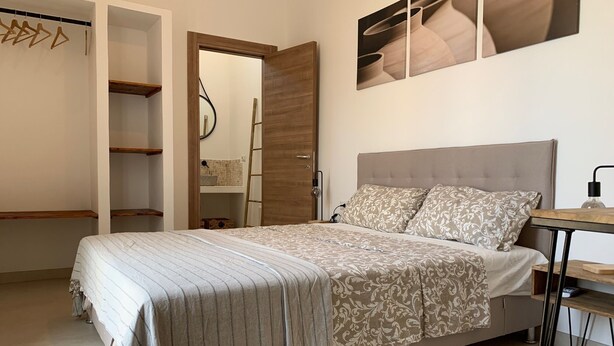 Un dormitorio con cama, un armario de madera, una escalera y una estantería fijada a la pared.