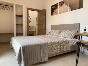 Quarto com cama, guarda-roupa de madeira, escada e prateleira na parede.