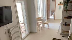 Una sala moderna con un televisor de pantalla plana, un banco de madera, un sofá verde y un comedor con mesa y sillas.