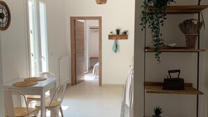 Un comedor amplio con una mesa y sillas blancas, un lámpara colgante y una estantería de madera con plantas.