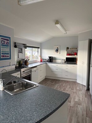 A modern kitchen with a granite countertop, stainless steel appliances, and a window providing natural light. - Hosts on the Coast - Catch of the Day (Cooks Beach)