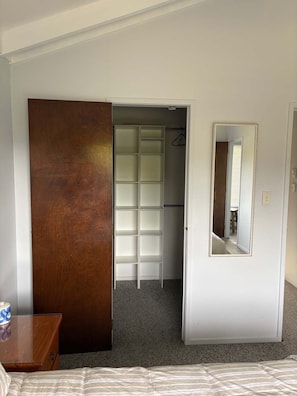 Une chambre à coucher comprenant un lit, une armoire en bois, un placard avec des étagères et un miroir.