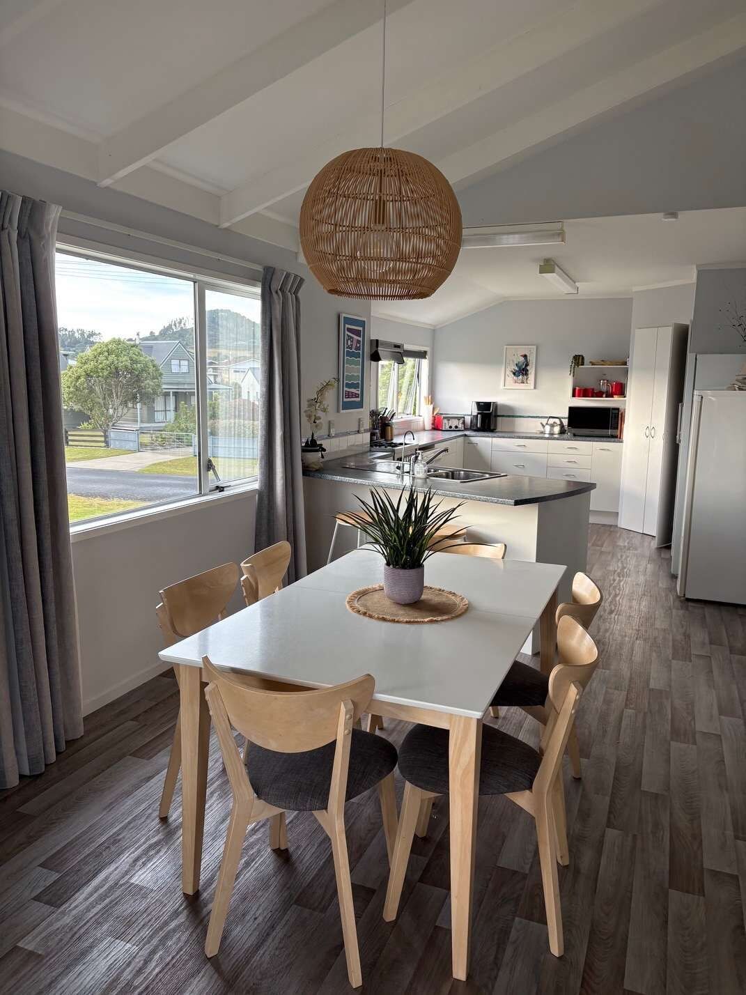 A modern kitchen with a central island, a dining area with a table and chairs, and a large window with curtains.