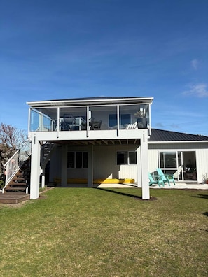 A two-story house with a covered patio area, a staircase leading to the upper level, and a sliding glass door leading to a garage. - Hosts on the Coast - Catch of the Day (Cooks Beach)