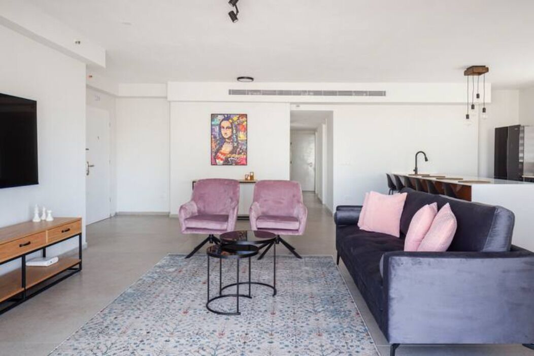 A modern living room with a dark sofa, two pink armchairs, a coffee table, and a TV on a wooden console.