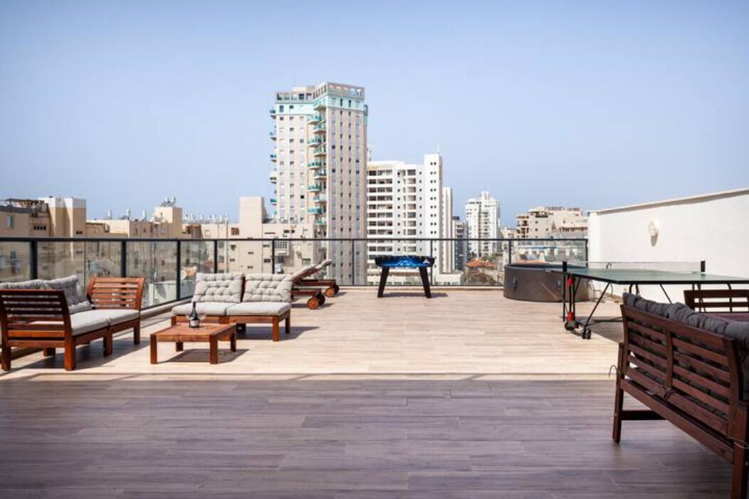 A rooftop terrace with outdoor furniture, a ping pong table, and a view of surrounding buildings.