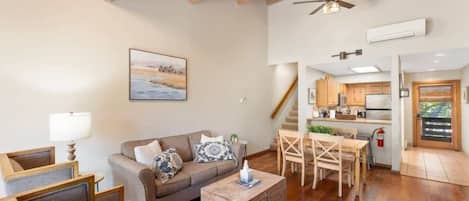 A spacious living area with a wooden ceiling, a sofa with cushions, a coffee table, and a dining table with chairs.