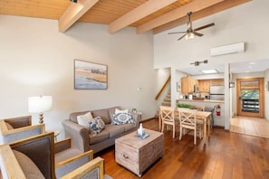 A spacious living area with a wooden ceiling, a sofa with cushions, a coffee table, and a dining table with chairs.