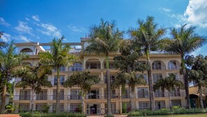 A multi-story hotel with a central courtyard, surrounded by palm trees and a clear blue sky.