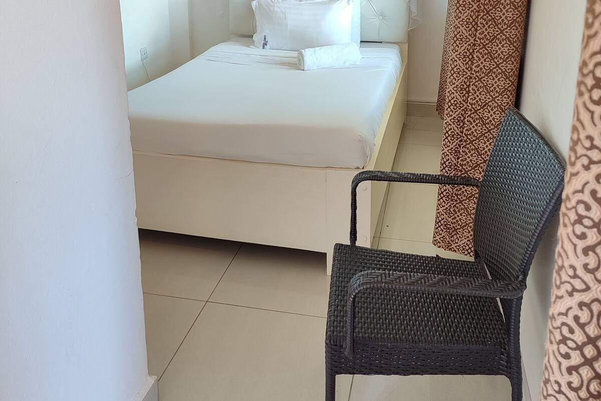 A bedroom with a bed, white bedding, a canopy, a chair, and patterned curtains.