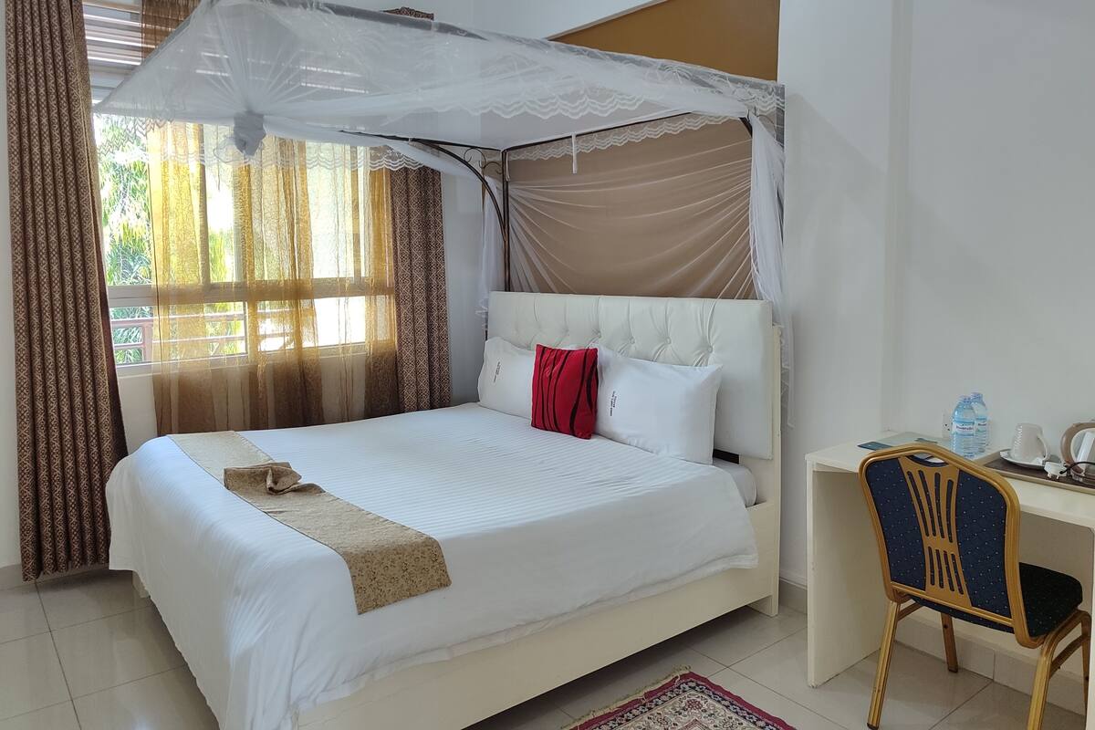 A neatly made bed with a canopy, a desk with a chair, and a water bottle on the desk.