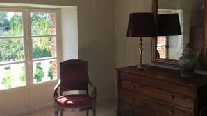 Ein Zimmer mit einem Holzkleiderschrank, einem Stuhl, einem Spiegel und einem Fenster mit Blick auf Grünflächen.
