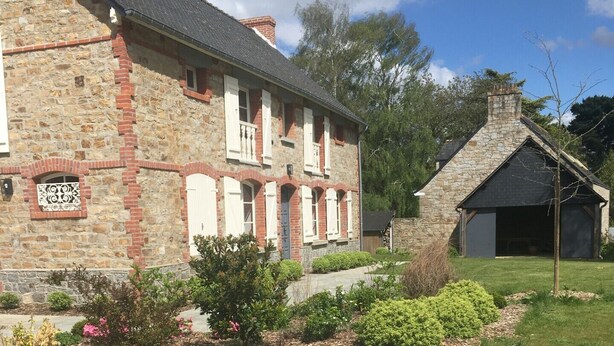 Ein Steinhaus mit gepflastertem Innenhof, einem kleinen Garten mit rosa Blüten und einem Schornstein.
