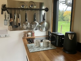 Una cocina con ollas y sartenes colgando, una cafetera, un tostador y una ventana con vistas al verdor.