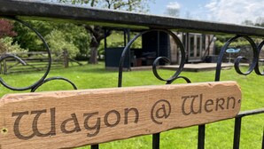 Une pancarte en bois portant l’inscription « Wagon @ Wiern » est fixée à une clôture métallique.