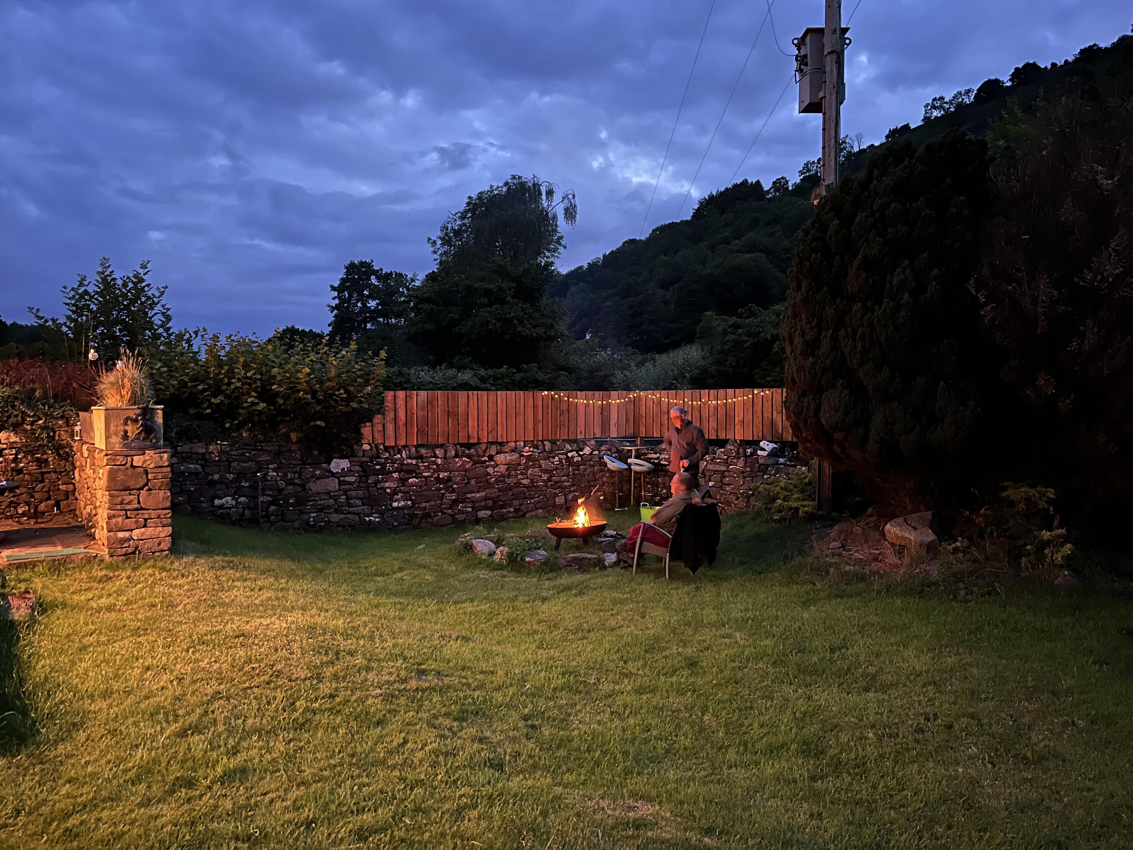 A stone wall, a wooden fence, and a grassy yard with a fire pit.