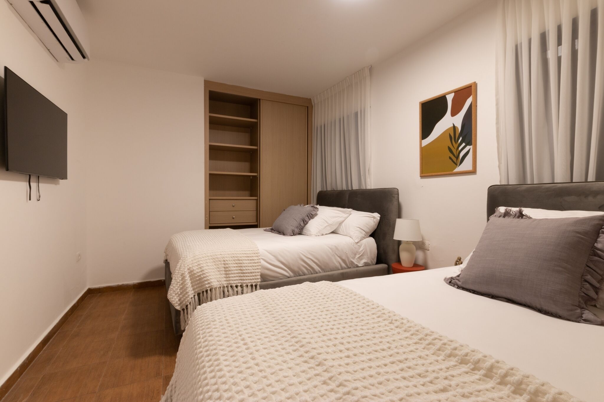 A hotel room with two beds, a wardrobe, a flat-screen TV, and a painting on the wall.