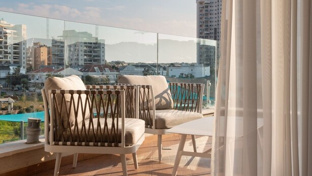 Un balcón con vistas a un paisaje urbano, con una silla acolchada y una mesita.