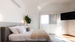 Un dormitorio moderno con una cama grande, una planta en maceta y un televisor en la pared.