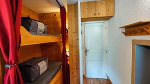 A compact room with a bunk bed, a small seating area, and a white door. - Charming 19m² Studio for 3 with Terrace and Parking, 5min from Shops & Free Shuttle (Arêches-Beaufort)