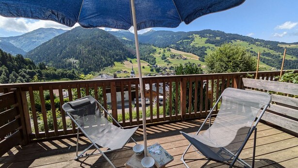 A wooden deck with two metal chairs and a table, an umbrella, and a scenic mountain view. - Charming 19m² Studio for 3 with Terrace and Parking, 5min from Shops & Free Shuttle (Arêches-Beaufort)