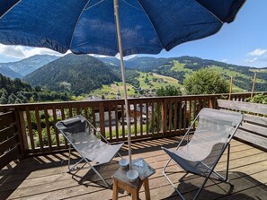 A wooden deck with two metal chairs and a table, an umbrella, and a scenic mountain view. - Charming 19m² Studio for 3 with Terrace and Parking, 5min from Shops & Free Shuttle (Arêches-Beaufort)