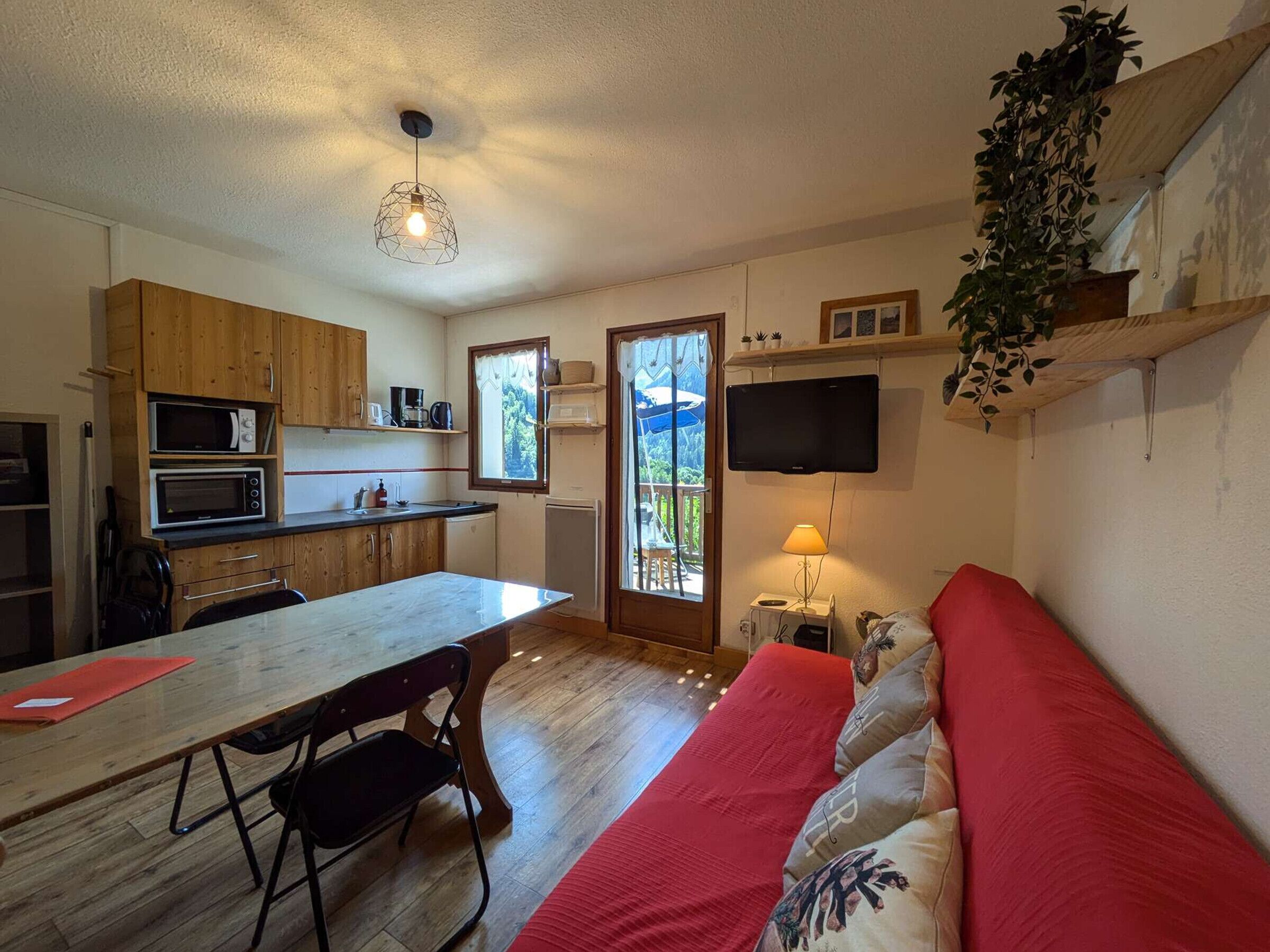 Ein gemütlicher Wohnraum mit Küchenzeile, Essbereich, Sofa und an der Wand montiertem Fernseher.