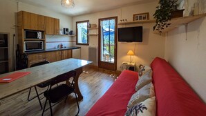 A compact living space with a kitchenette, a dining area, a sofa, and a TV mounted on the wall. - Charming 19m² Studio for 3 with Terrace and Parking, 5min from Shops & Free Shuttle (Arêches-Beaufort)