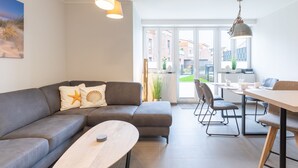 A modern living room with a grey sofa, a round coffee table, and a dining area with a table and chairs. - Ferienhaus Westwind in Tönning für bis zu 4 Personen (Tönning)