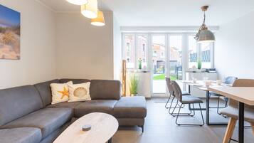Ein modernes Wohnzimmer mit einem grauen Sofa, einem runden Couchtisch und einem Essbereich mit Tisch und Stühlen.