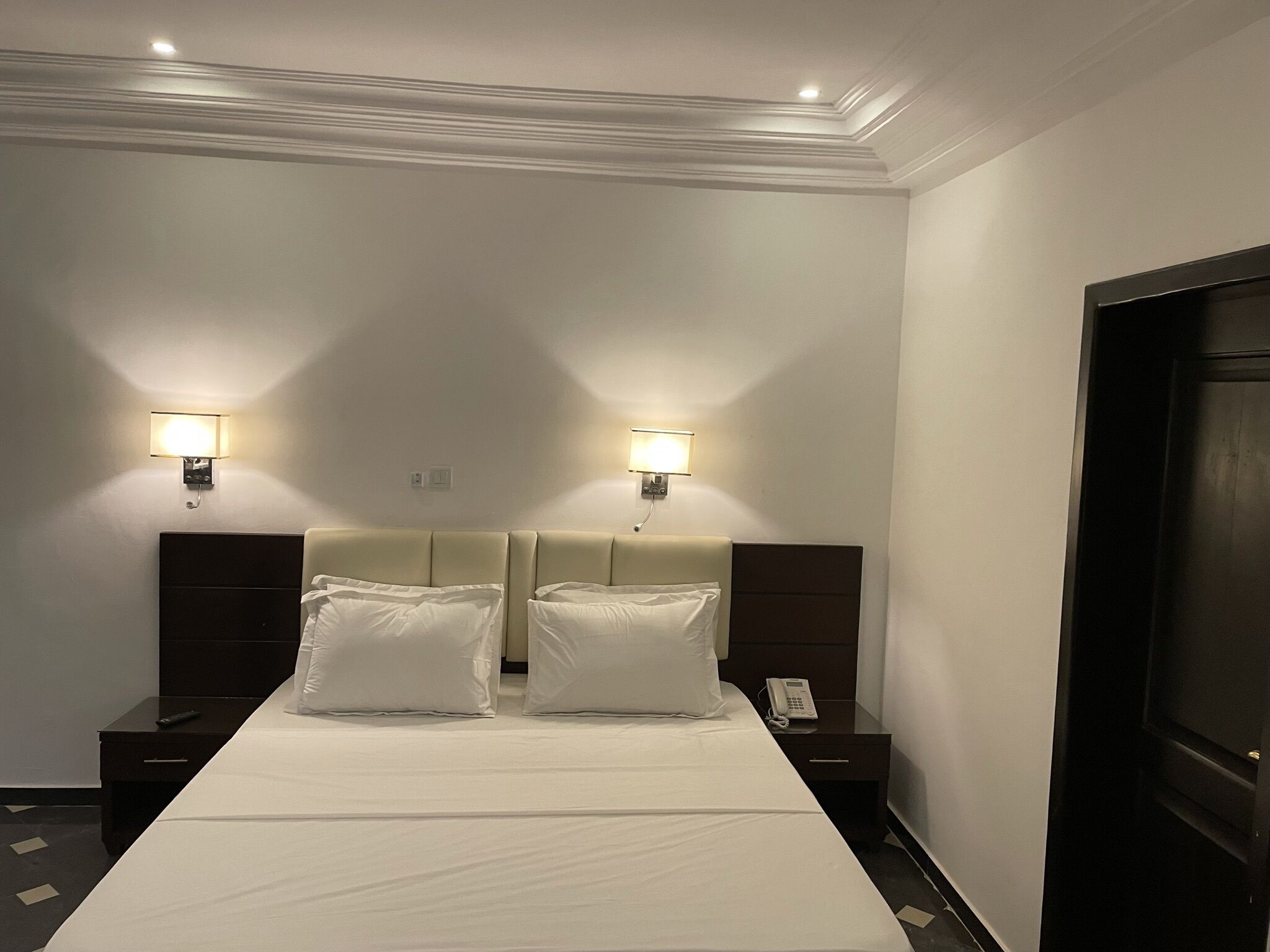 Una habitación de hotel con una cama grande, dos mesitas de noche, un teléfono y dos lámparas fijadas a la pared.