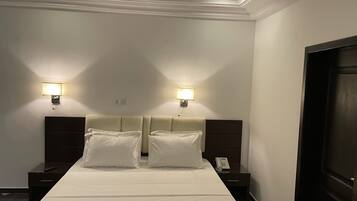 Una habitación de hotel con una cama grande, dos mesitas de noche, un teléfono y dos lámparas fijadas a la pared.