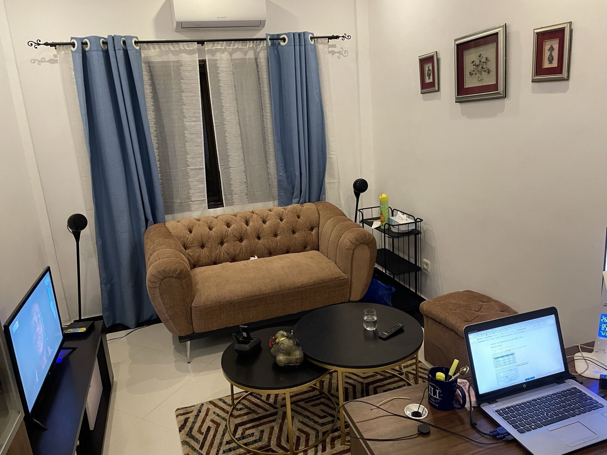 A living room with a brown sofa, a small round table, a laptop, and a TV.