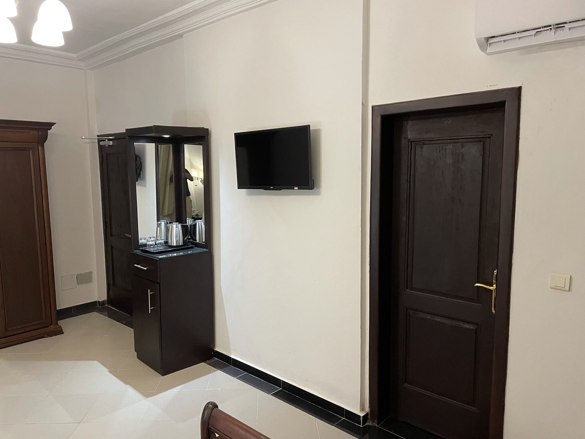 Ein Hotelzimmer mit einer dunklen Holztür, einem an der Wand montierten Flachbildfernseher und einem dunklen Holzschrank mit Spiegel und Kaffeemaschine.