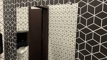 Ein Badezimmer mit einer Wand mit geometrischem Muster, einem dunkelbraunen, vertikalen Objekt und einem Papierhandtuchspender.