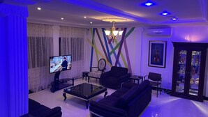 Una sala de estar moderna con un televisor de pantalla plana, sofás negros, una mesa de centro y una araña.