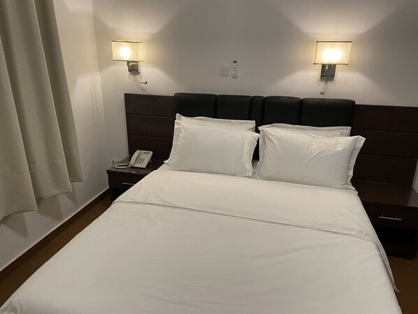 Una habitación de hotel con una cama grande, dos lámparas de noche, un teléfono junto a la cama y una mesita de noche.