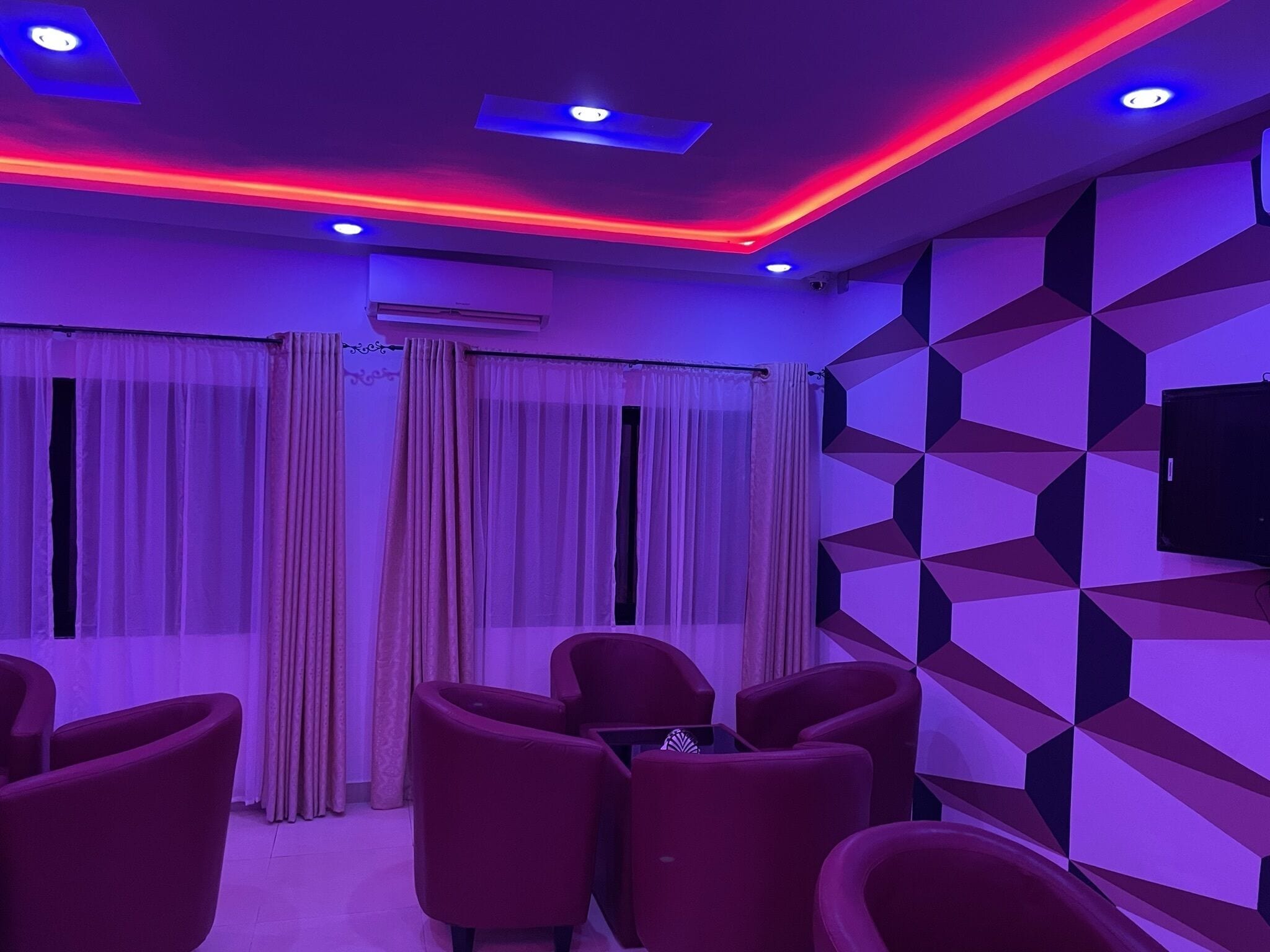 A room with red chairs, a geometric patterned wall, and a ceiling with red and blue lighting.