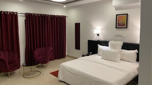 Habitación de hotel con cama, mesita de noche, lámpara, sillón y cortinas.